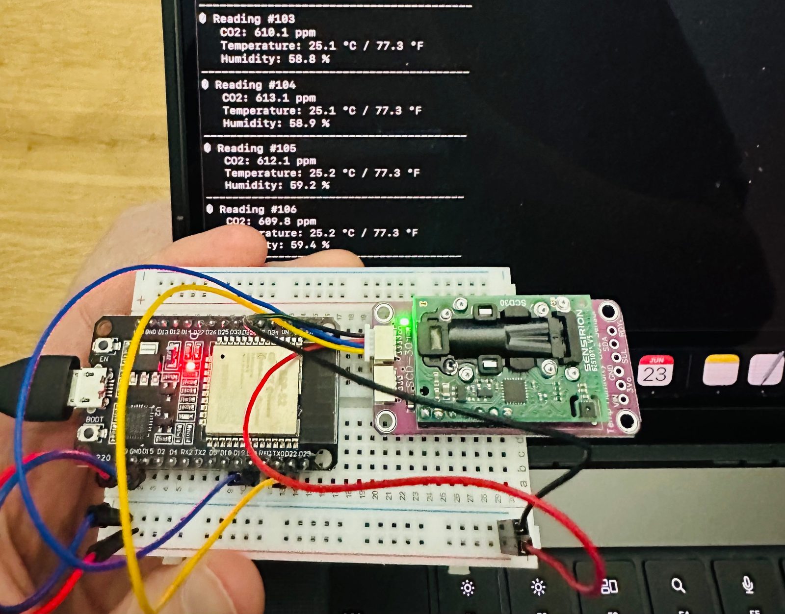 A breadboard sensor prototype with a CO2 sensor, next to a laptop printing CO2, temperature and humidity readings